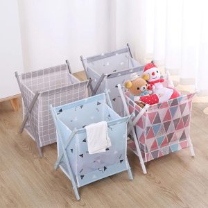 Four foldable laundry baskets in different patterns (gray grid, blue geometric, pink geometric, and light gray) arranged on a wooden floor. The baskets are shown being used as storage hampers for clothes and plush toys, highlighting their large capacity and versatile design for home organization.