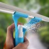 A hand holds a light blue 3-in-1 Wonder Spray Window Squeegee with a Glass Cleaning Wiper Blade as its built-in spray bottle emits a fine mist of liquid.