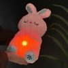 The soft pink Plush Breathing Cute Rabbit Toy with Sensory Electronic Soft Tech features embroidered sleeping eyes, teal-accented paws with a music note icon, and a glowing warm orange belly light.